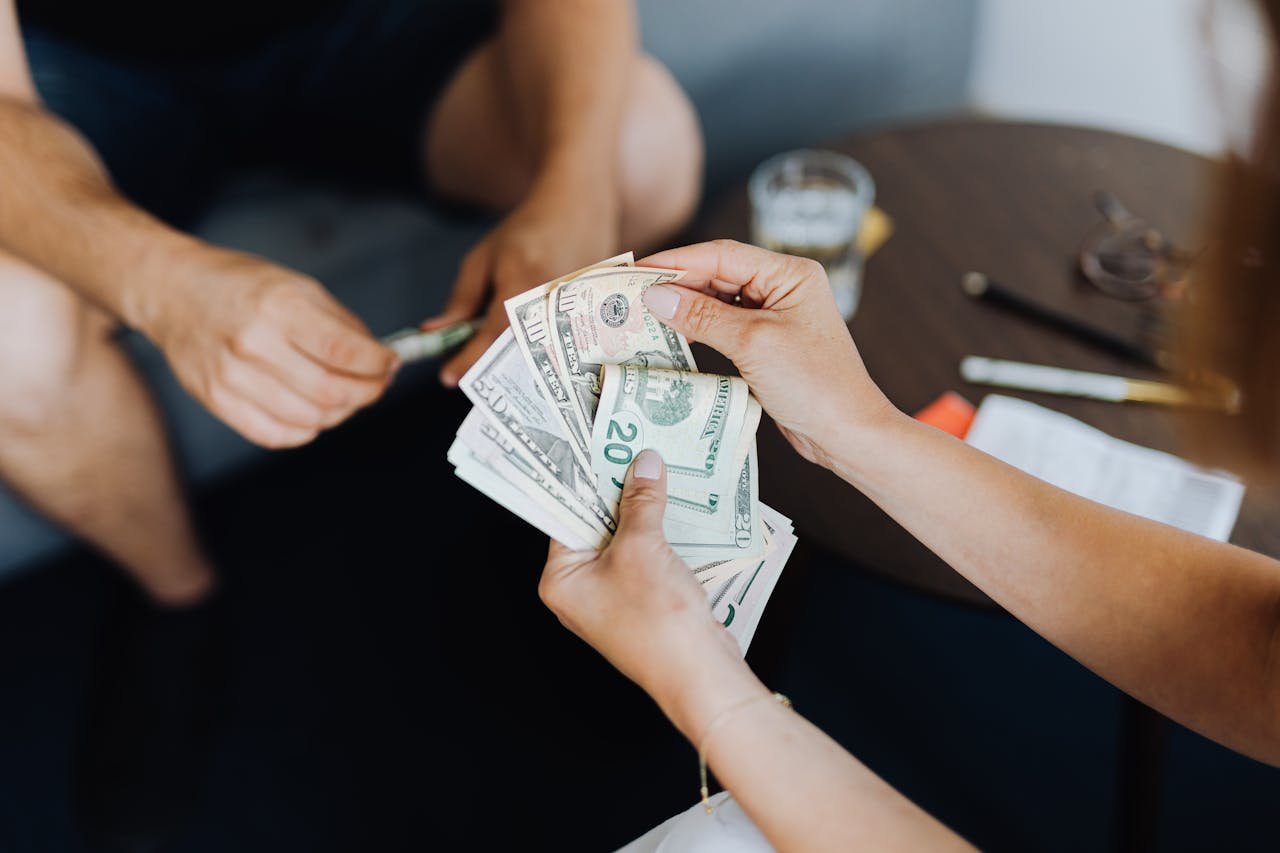 Close-up of people handling and counting US dollar bills indoors.